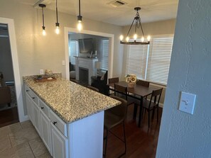 A kitchen with a granite countertop, white cabinets, and a dining area with a table and chairs. - Mulberry Cottage - Your Cozy Home Away from Home (Amarillo)