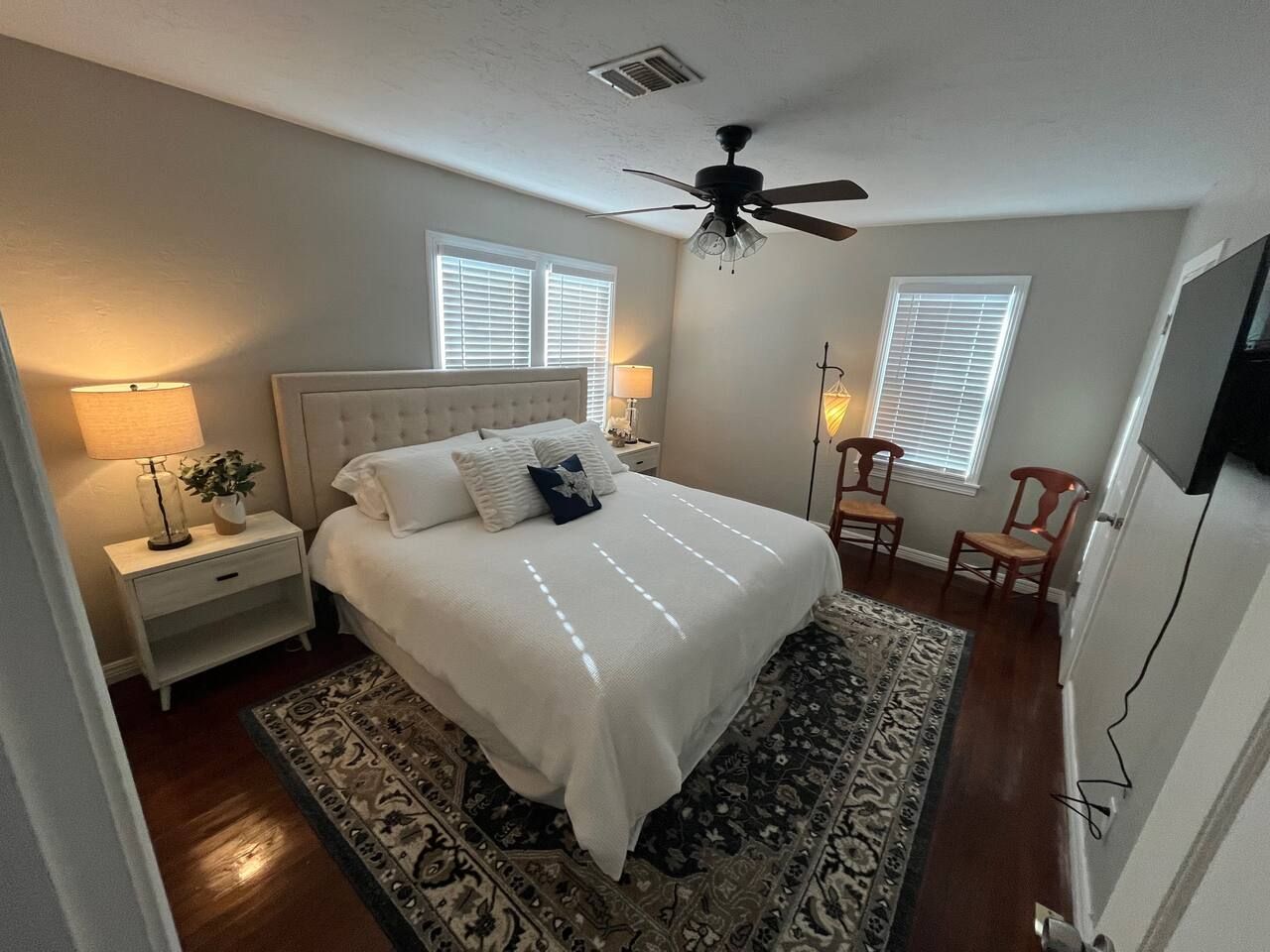 A bedroom with a large bed, two bedside lamps, a ceiling fan, and a patterned rug.