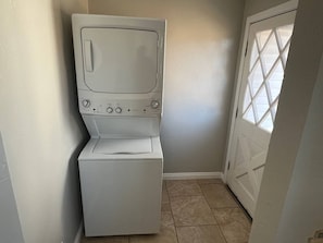 A laundry area with a front-loading washer and dryer, a white door with a diamond pattern, and a tiled floor.