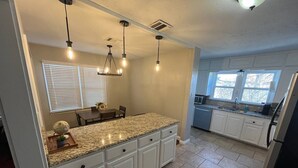 Cocina con encimera de granito, armarios blancos e iluminación colgante.