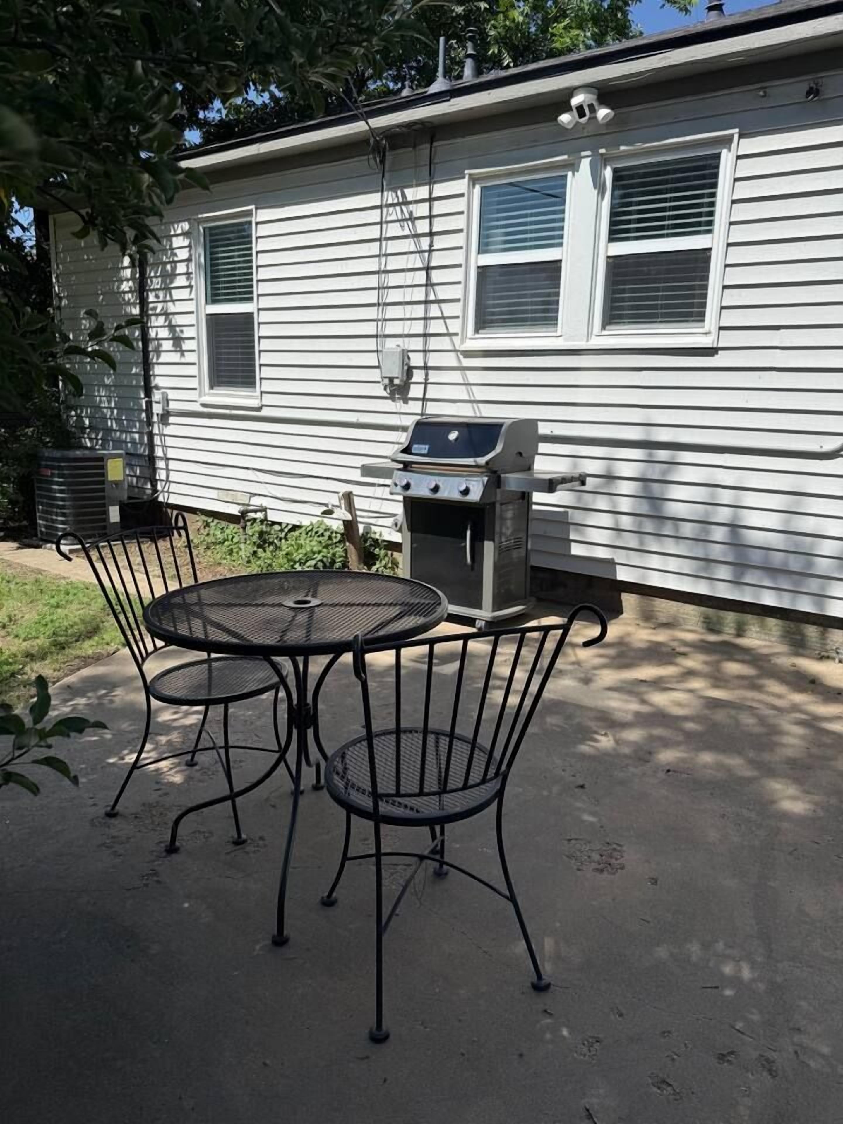 A patio with a grill and metal chairs in front of a house.