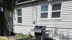 Un patio con una parrilla y sillas metálicas frente a una casa.