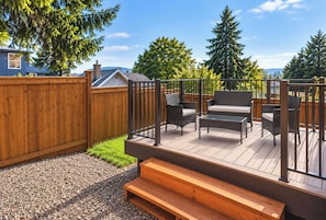 Une terrasse en bois avec des meubles d’extérieur, une clôture en bois et une zone recouverte de gravier.
