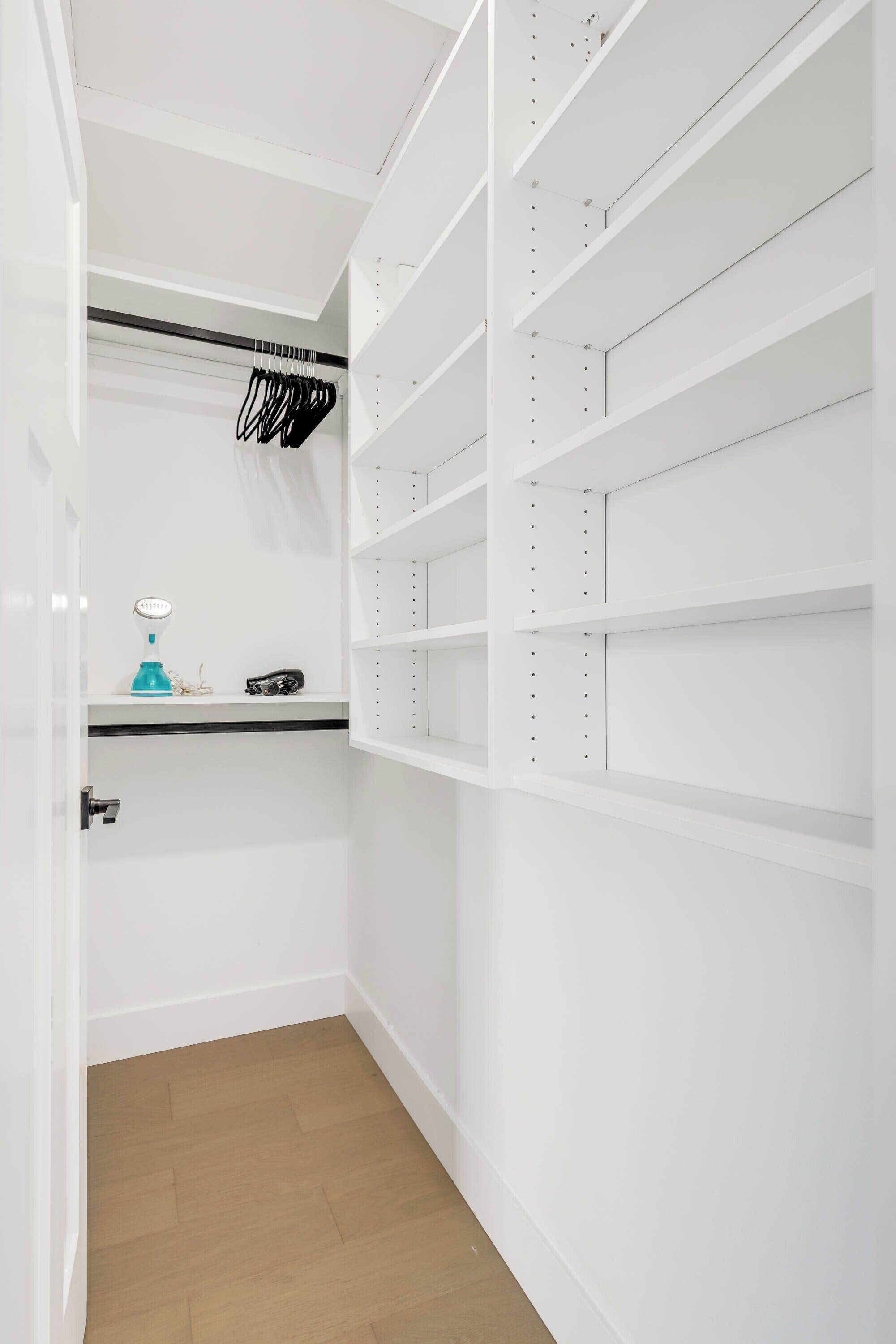 Ein weißer Kleiderschrank mit Regalen und Kleiderstange, ein blaues Objekt auf der unteren Ablage und eine Tür mit Griff.