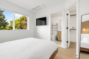 Een moderne slaapkamer met een groot bed, een aan de muur bevestigde televisie en uitzicht op bomen.