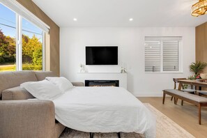 Een moderne slaapkamer met een groot bed, een flatscreen televisie erboven, een open haard en een zithoek met een bank.