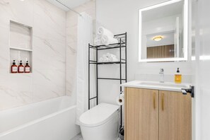 Een moderne badkamer met een wit toilet, een houten kastje, een plank met toiletartikelen en een handdoekrek.
