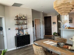 Een eetgedeelte met een houten tafel, rieten stoelen, een zwarte console en een decoratieve kroonluchter.
