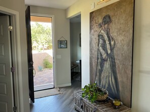 An interior hallway with a door leading outside, a large abstract painting on the wall, a wicker basket with a plant, and a small table with a vase. - Starlit Tubac Home , with a Golf Cart! (Tubac)