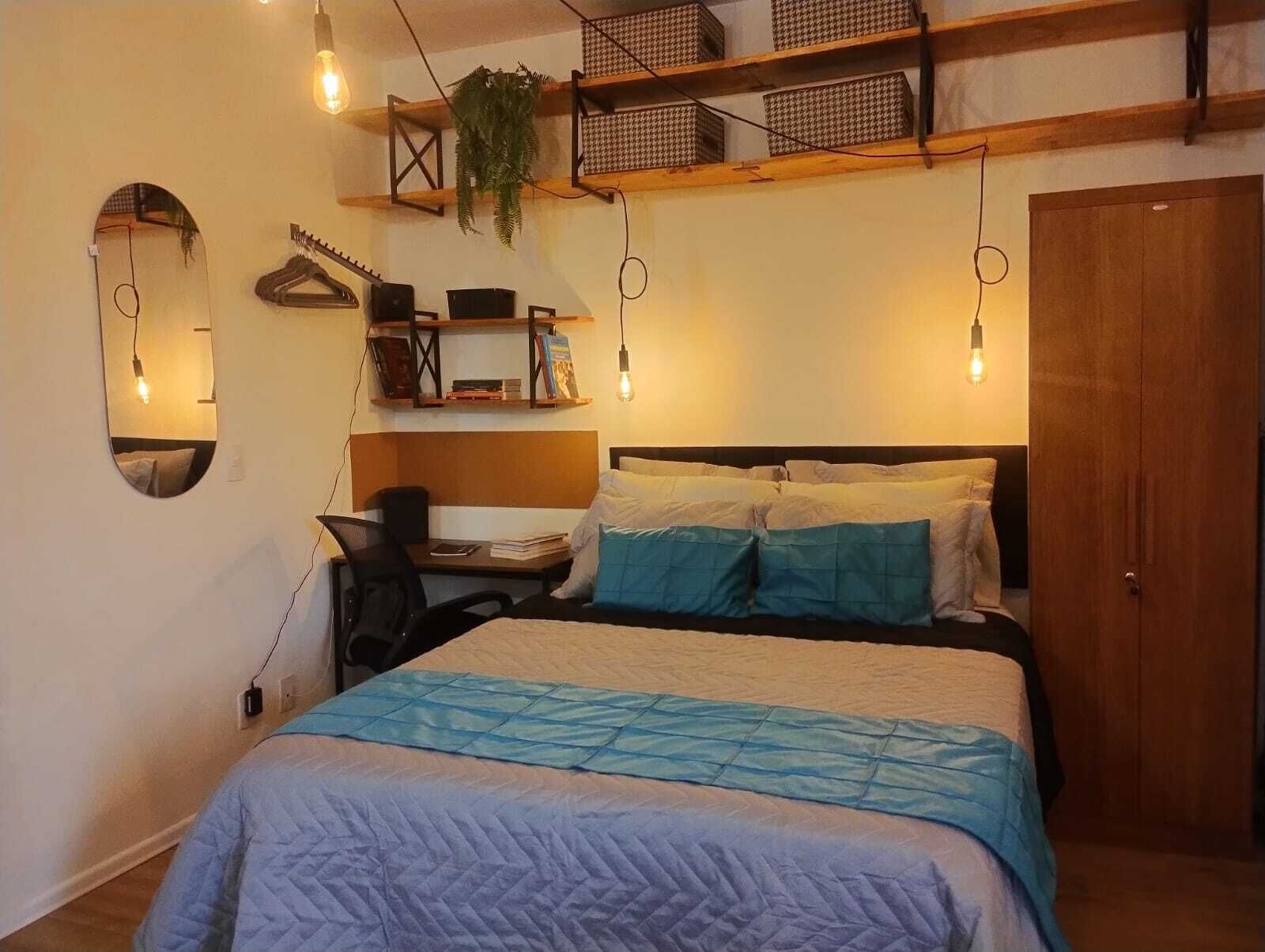 Un dormitorio con una cama, un escritorio, una silla, un espejo y estantes con objetos.