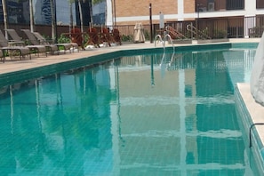 A swimming pool with clear water, surrounded by lounge chairs and a building in the background. - Fully equipped studio apartment in Rio with free parking, great location. (Rio de Janeiro)
