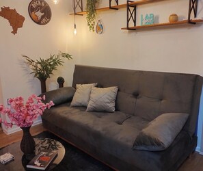 Ein modernes Wohnzimmer mit einem grauen Sofa, zwei Kissen, einem kleinen Topfpflanzen und einem dekorativen Globus sowie einem an der Wand befestigten Regal mit Gegenständen.