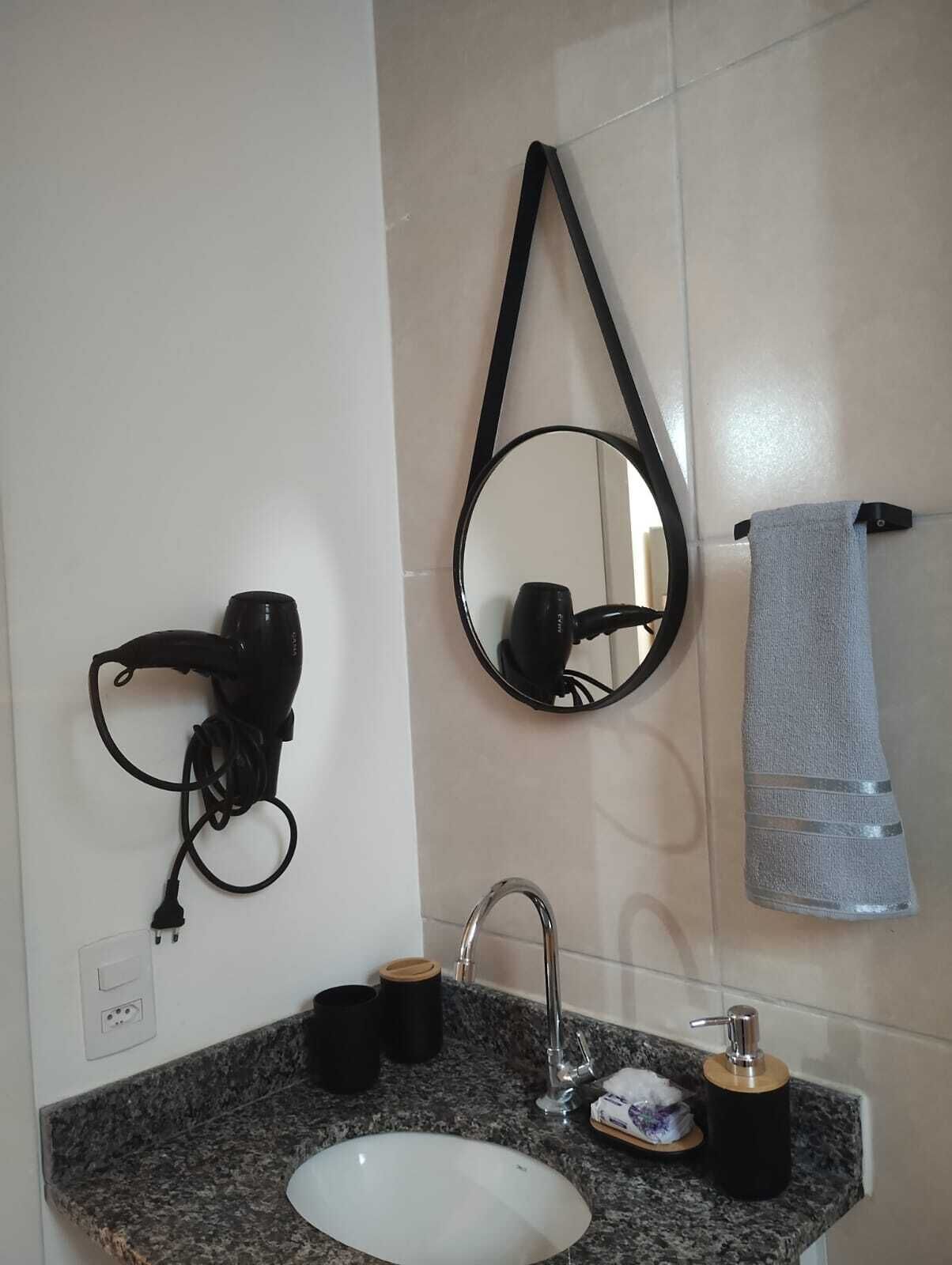 A bathroom with a sink, faucet, hairdryer, mirror, towel, and a small soap dispenser.