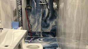 A bathroom with a marble floor, a toilet, a sink, and a shower area. - Wembley Park - Free Parking (London)