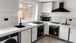 A modern kitchen with a built-in washer, double sink, microwave, oven, and a black range hood. - Wembley Park - Free Parking (London)