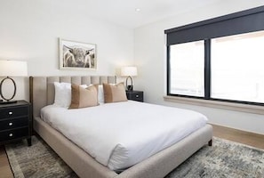 A bedroom with a large bed, two bedside tables, a nightstand, a framed picture on the wall, and a window with blinds. - Riverwood Ten Lux Poolside Ski In/Out to BC Westin Resort Amenities (Avon)