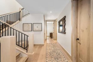 A hallway with a wooden floor, a rug, a staircase with black railings, and a door with a mirror. - Riverwood Ten Lux Poolside Ski In/Out to BC Westin Resort Amenities (Avon)