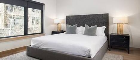 A modern bedroom with a large bed, two bedside tables, and a view through a window.