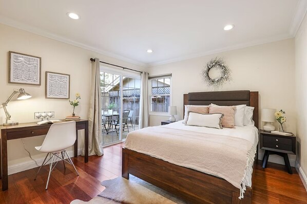 A bedroom with a bed, desk, chair, and a view to an outdoor patio.