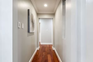 A hallway with a wooden floor, white walls, and a ceiling light.