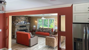 A living room with a stone fireplace, red sofas, and a kitchen with stainless steel appliances.
