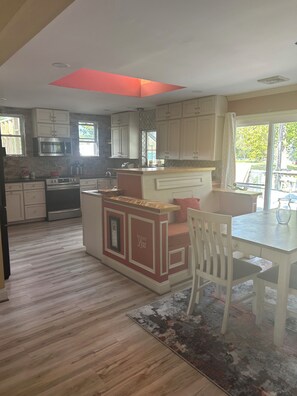 A modern kitchen with white cabinetry, a central island, and a dining area with a white chair. - Luxury 3,000 Sq Ft Multi‑Suite Retreat • Designer Interiors • Workspaces (Welcome)