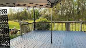 A wooden deck with a metal railing, a covered area with a roof, and a view of a grassy yard with trees.