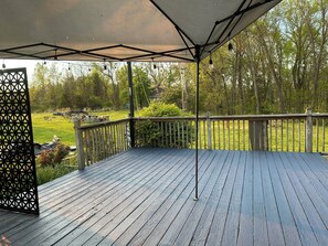 A wooden deck with a metal railing, a covered area with a roof, and a view of a grassy yard with trees.