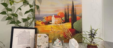 A wall with a framed map, a framed inspirational quote, a decorative pine cone arrangement, and a potted plant.