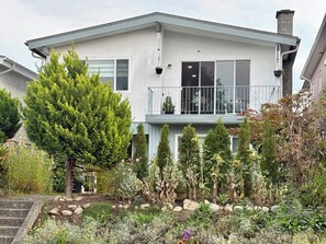 A two-story house with a balcony, surrounded by a garden with various plants and flowers. - Family-Friendly 2 Bedroom Sweethome Sleeps 6 + Free Parking (Vancouver)