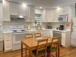 A modern kitchen with white cabinetry, a wooden dining table, and a built-in microwave. - Family-Friendly 2 Bedroom Sweethome Sleeps 6 + Free Parking (Vancouver)