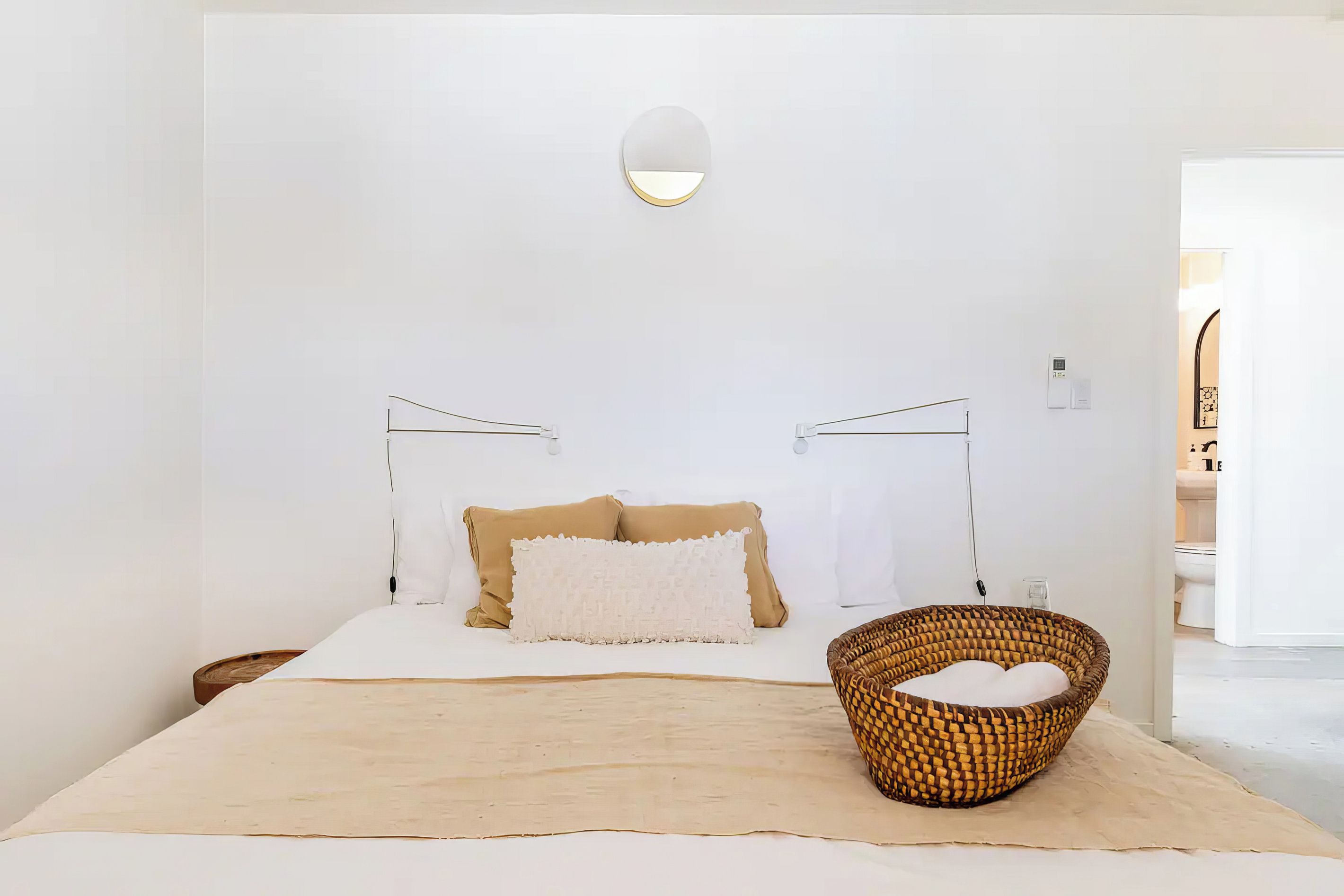 A minimalist bedroom with a bed, two bedside tables, a wall-mounted light, and a woven basket on the floor.