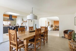 Un vaste espace de salle à manger avec une grande table et des chaises en bois, un luminaire suspendu moderne et une cuisine ouverte en arrière-plan.