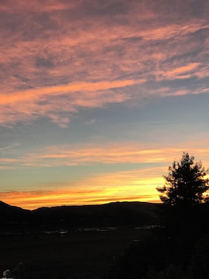 A sunset over a landscape with a silhouette of a tree and distant hills.