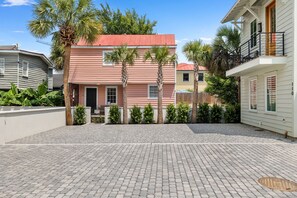 A paved courtyard with a pink building, palm trees, and a white building with a balcony. - Signature Residence @ Smalls Alley | Rooftop Deck (Charleston)
