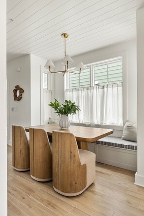 A dining area with a wooden table and chairs, a potted plant, and a window with curtains. - Signature Residence @ Smalls Alley | Rooftop Deck (Charleston)