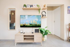 En moderne stue med et fladskærms-tv på væggen, et træskrivebord med en computer og en potteplante.