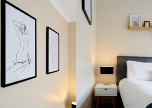Et hotelværelse med en seng, et natbord, en lampe og to billeder hængende på væggen.