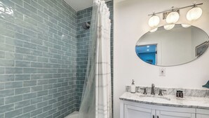 Um banheiro com chuveiro, pia com espelho e parede revestida de azulejos.