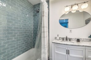 Ein Badezimmer mit Dusche, Waschbecken mit Spiegel und Fliesen.