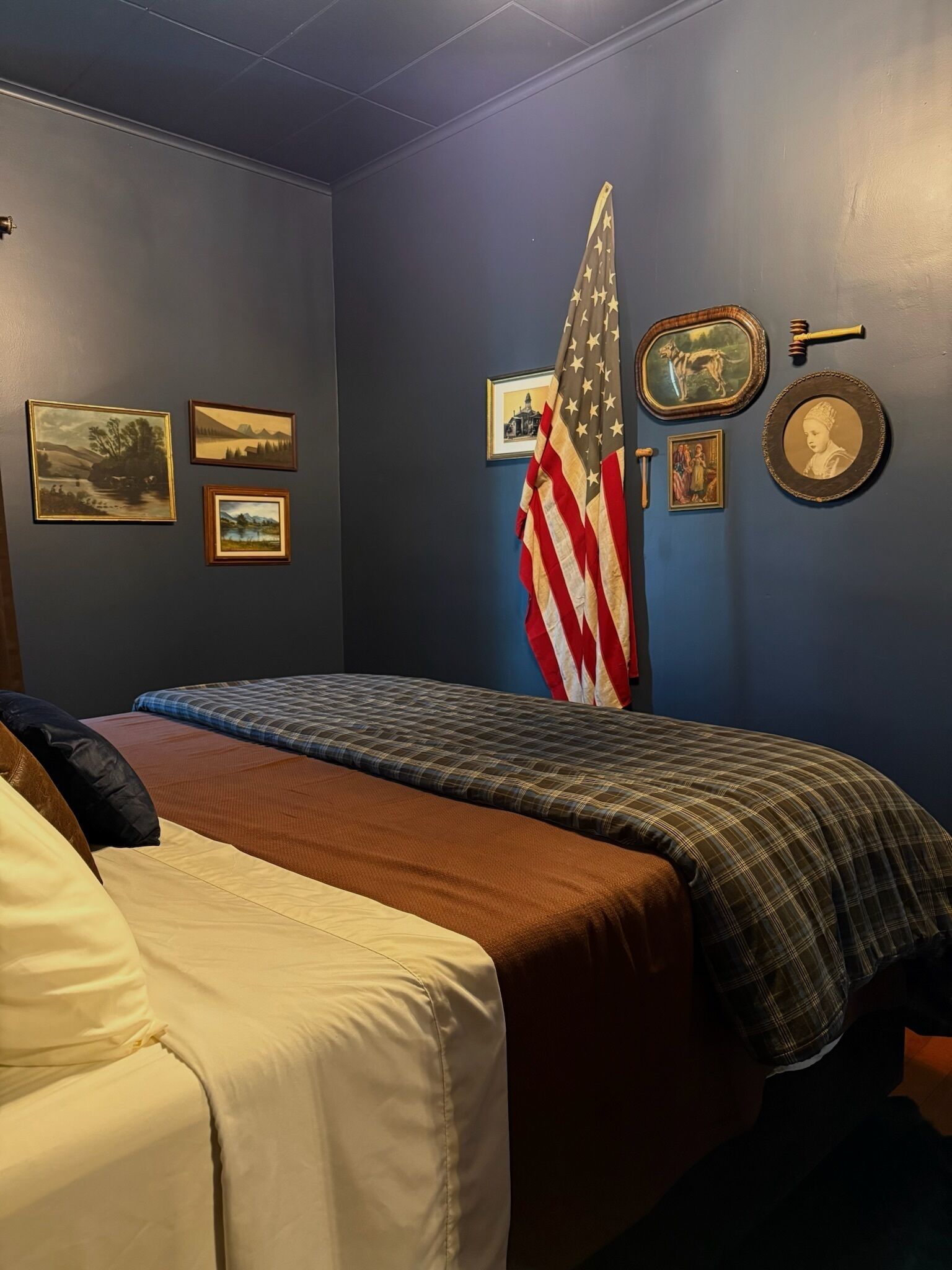 Um quarto com uma cama, uma parede com quadros, uma bandeira americana e uma chave na parede.
