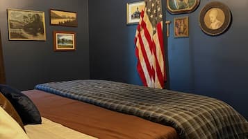 Un dormitorio con cama, una pared adornada con cuadros, una bandera estadounidense y una llave en la pared.
