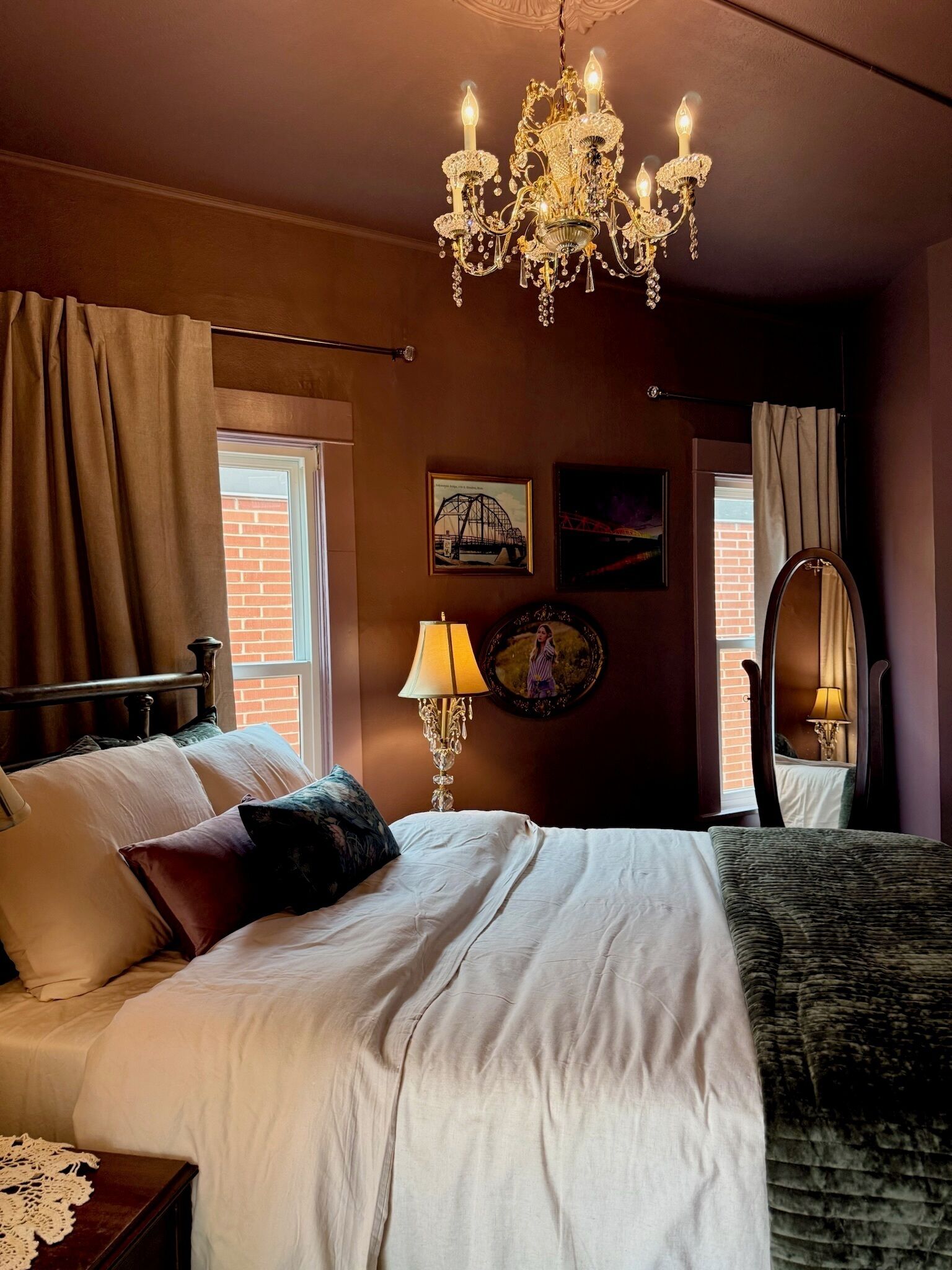 Une chambre à coucher avec un grand lit, un lustre, un miroir et des œuvres d’art accrochées aux murs.