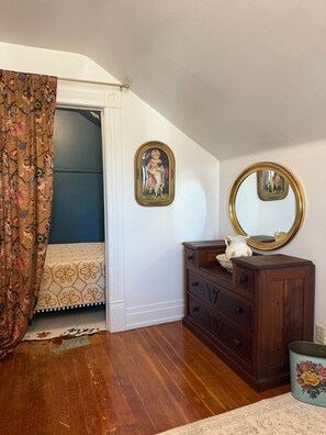 A bedroom with a wooden dresser, a mirror, a floral-patterned bed, and a door with a curtain.
