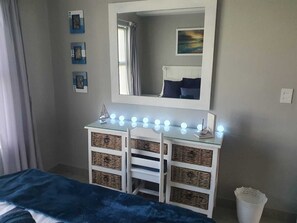 Ein Schlafzimmer mit einem Bett, einem Schminktisch mit Beleuchtung, einem Spiegel und einer Wand mit gerahmten Bildern.
