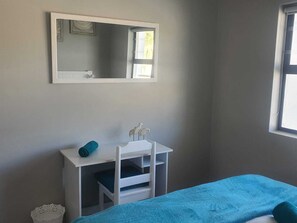 Una habitación con una cama, un escritorio blanco con una silla, un espejo y una ventana.
