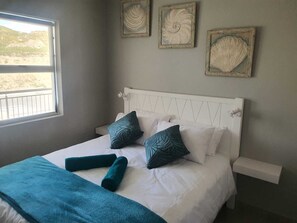 A bedroom with a bed, pillows, a blanket, and wall art. - Modern 2-bedroom apartment in Langebaan near the beach (Langebaan)