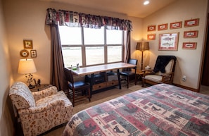 A hotel room with a large bed, a desk with two chairs, a lamp, and framed pictures on the wall. - Ennis Montana Cabin - Madison Range Views - 5 minutes to the Madison River (Ennis)