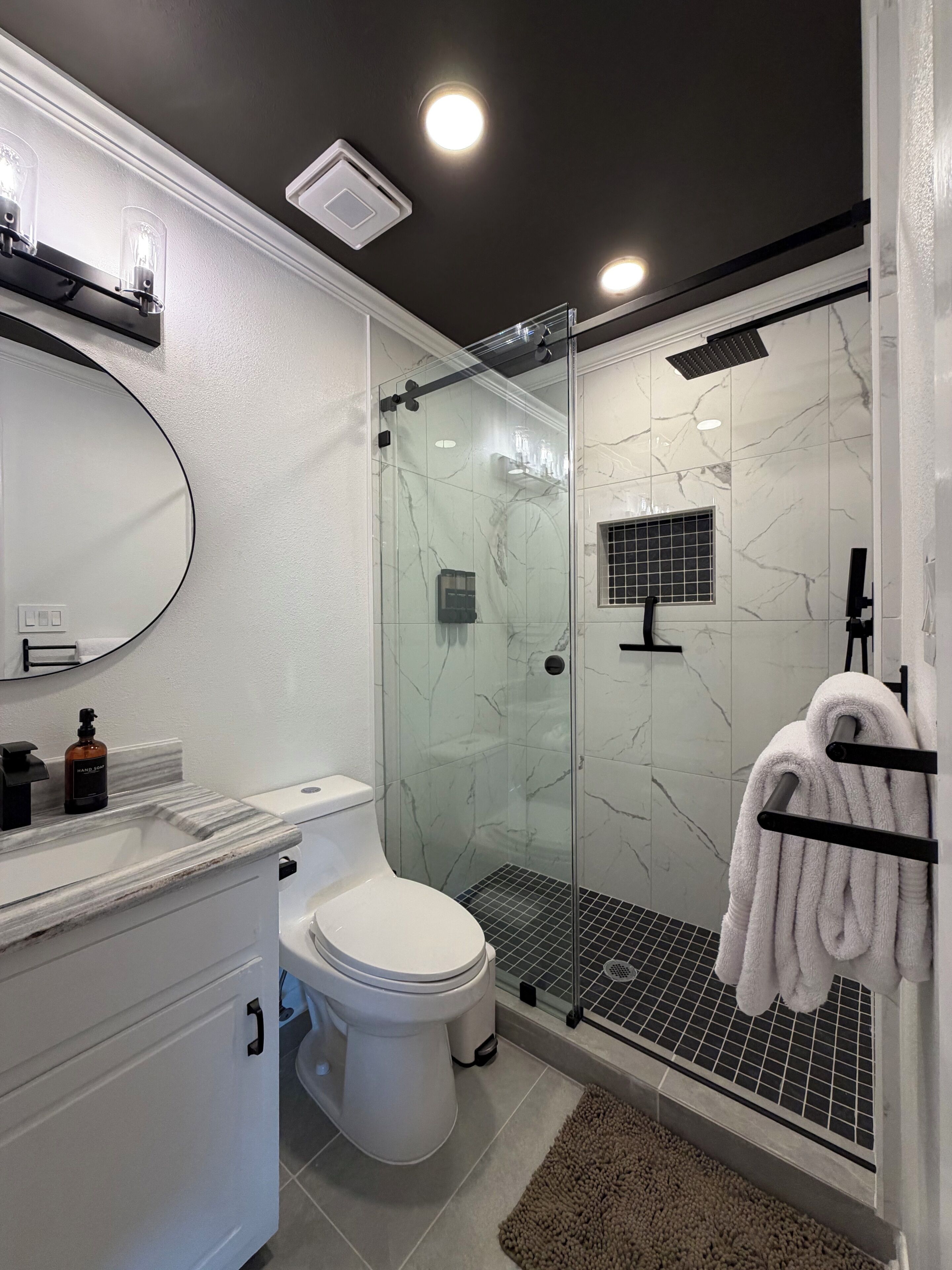 A modern bathroom with a glass-enclosed shower, a white toilet, and a vanity with a mirror.