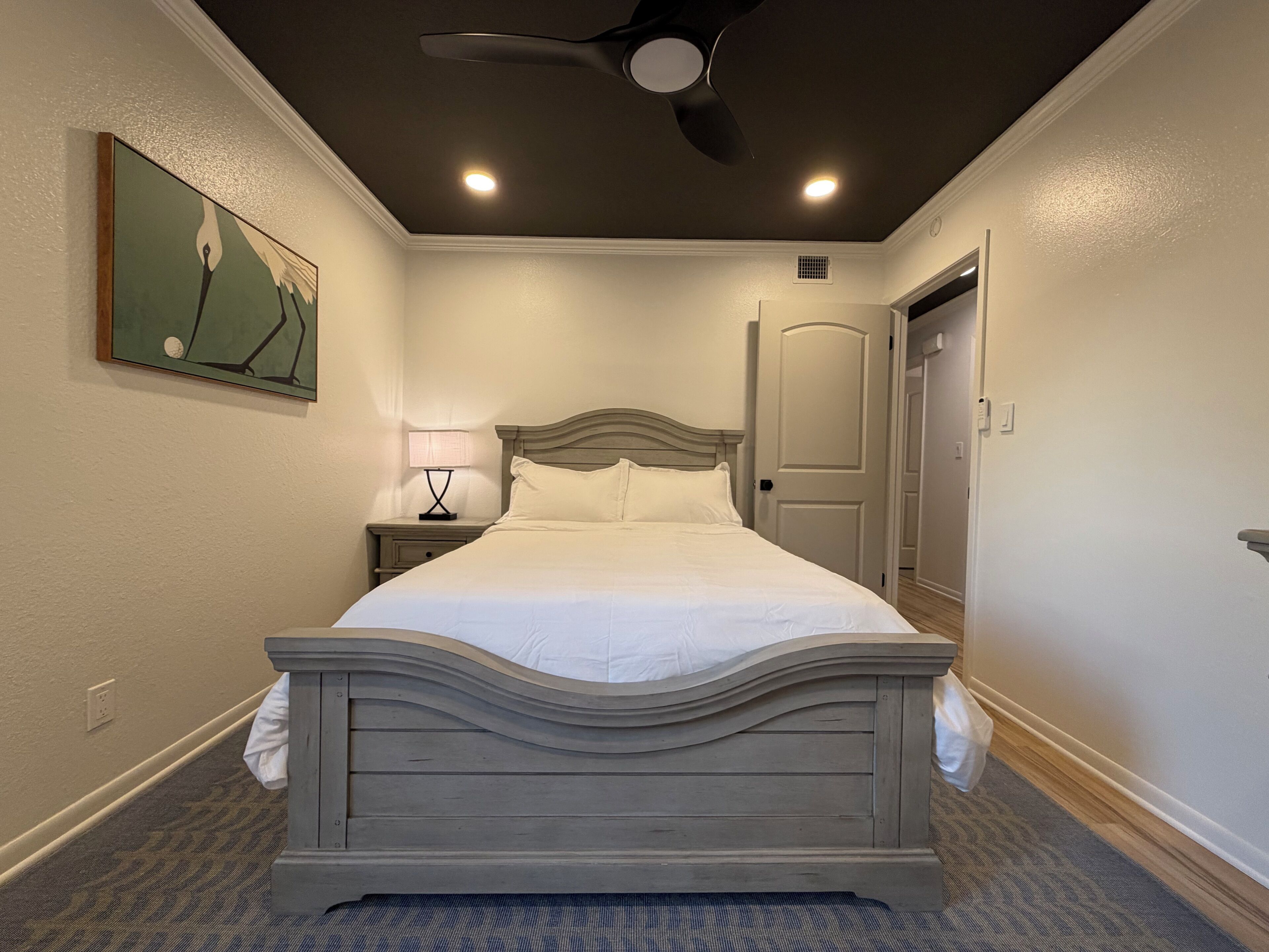 A hotel room with a bed, a nightstand, a ceiling fan, and a door.